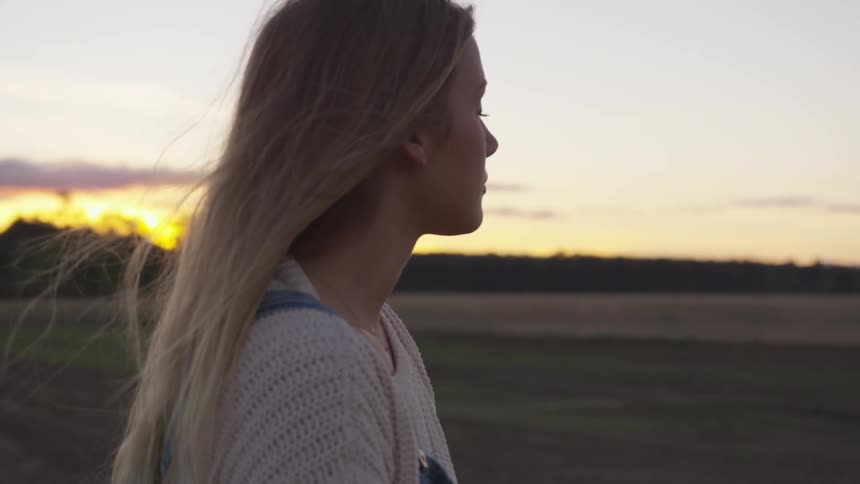 A woman stands in a rural field at sunset