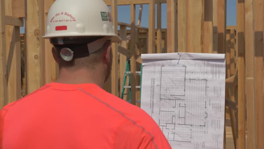A construction worker is reading blueprints posted on a wall outside in daylight