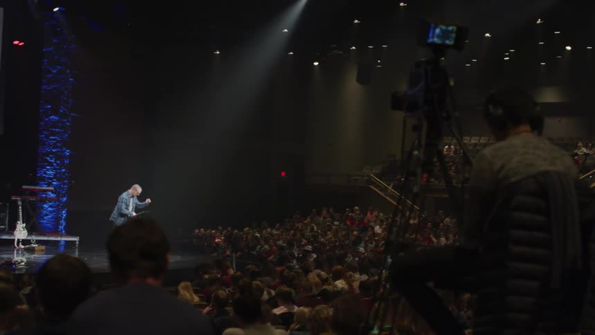 Man stands on stage talking in front of a large audience