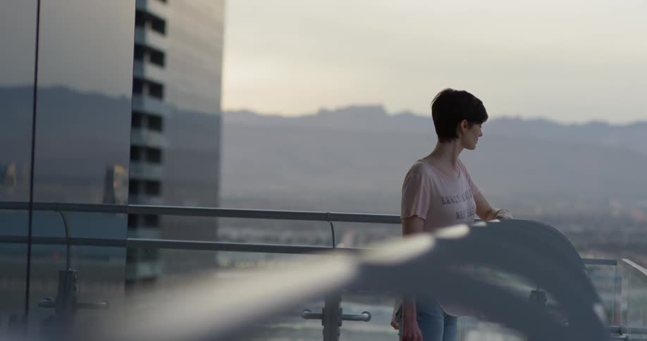 Woman stands on a balcony looking down at sunrise