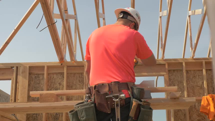 A construction worker works on building the frame of a building on a sunny day