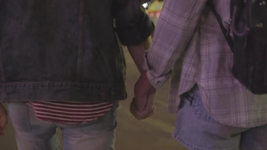 A couple are holding hands as they walk at a fair at dusk