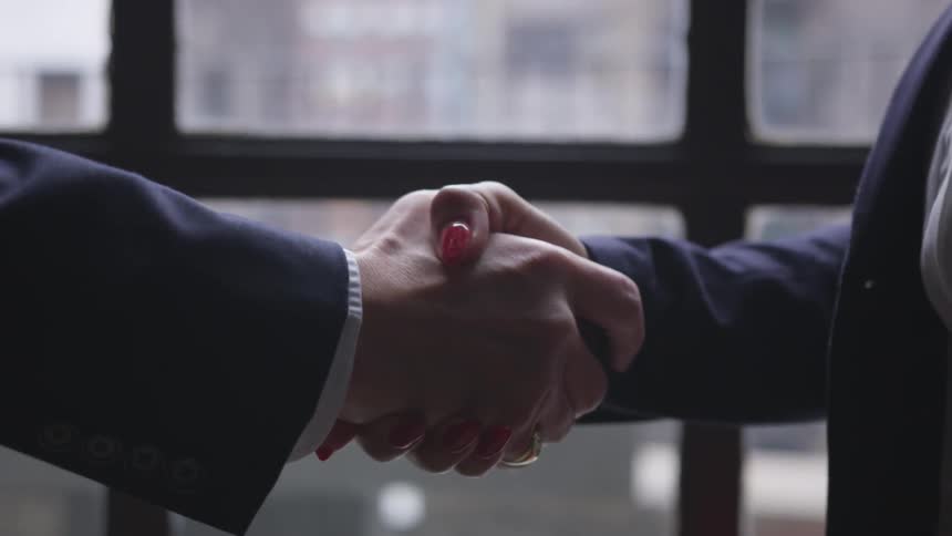 Two business professionals shake hands in front of a window