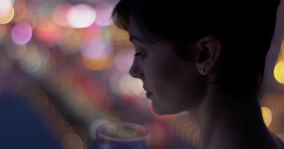 A woman has a drink at night above the city