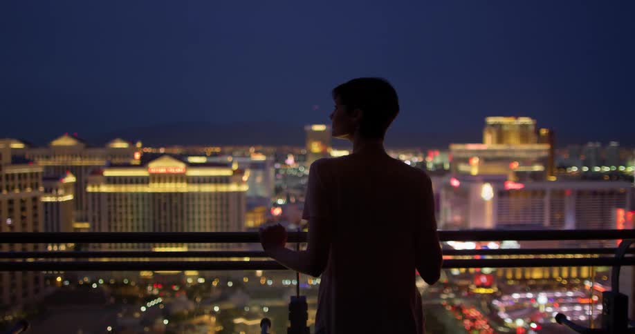 A woman walks out onto the balcony holding a drink