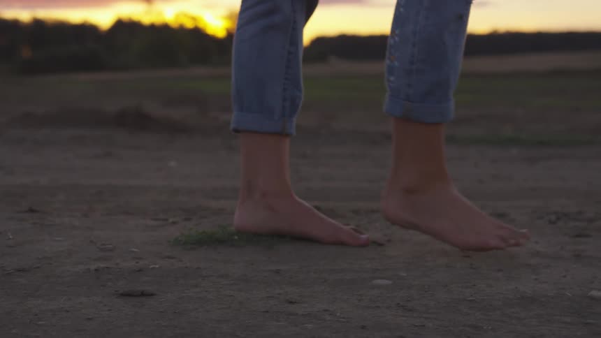 Woman walks barefoot on a path in the field