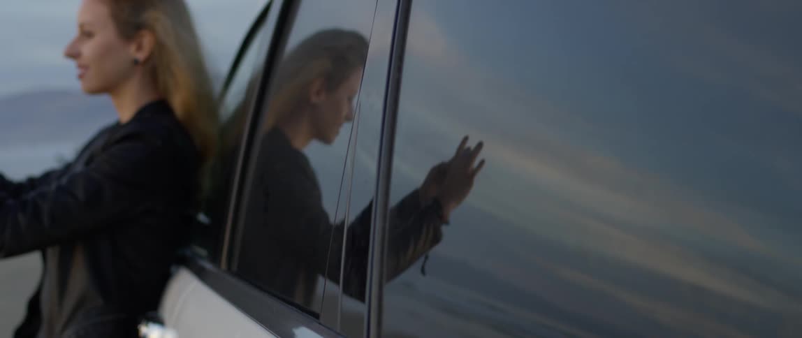 A woman is leaning against the car smiling