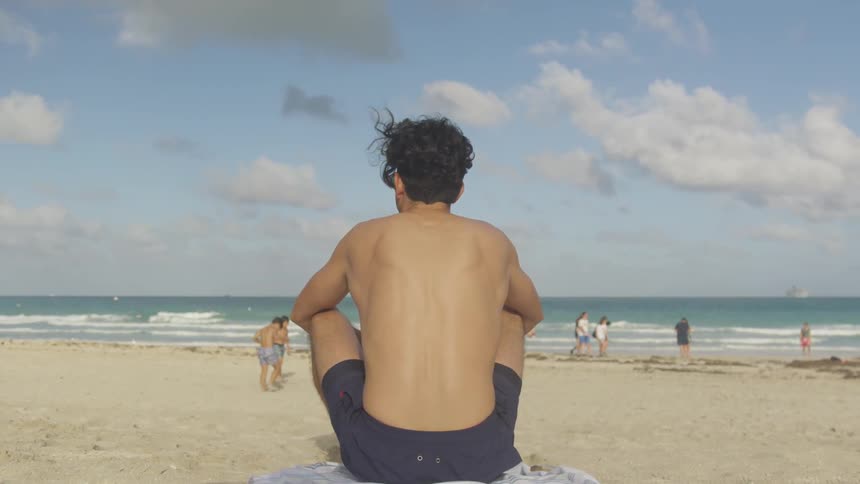 A man sits on the beach watching people and the waves