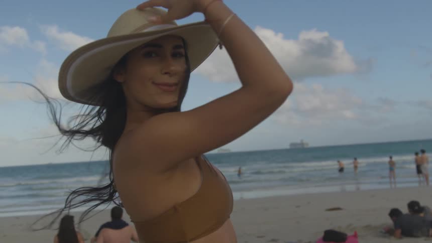 Woman holds her hat and spins around on the beach