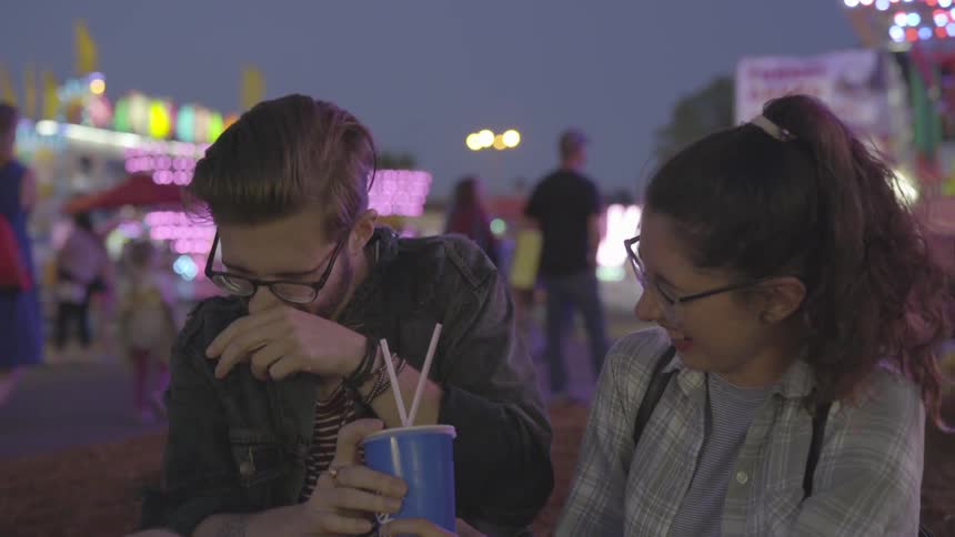 A man and woman share a drink at the carnival