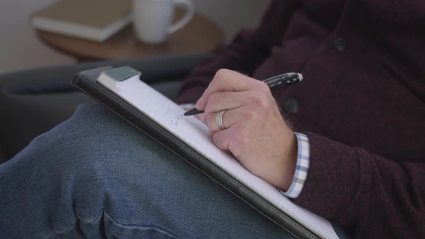 Person sits on a chair writing on a notepad