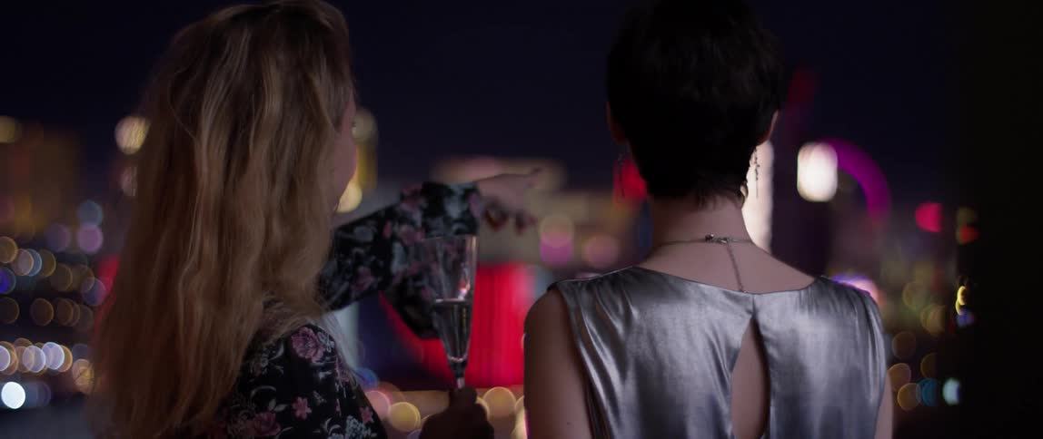 Two women watch the city at night from the balcony