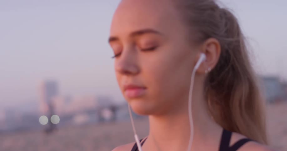 Woman wearing ear buds stands on the beach with her eyes closed