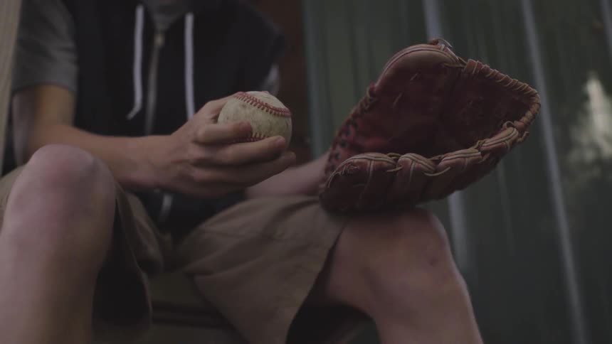A teenage boy holds a baseball and mitt