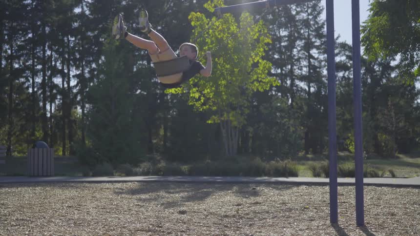 A little boy swings high on a swing with trees behind him