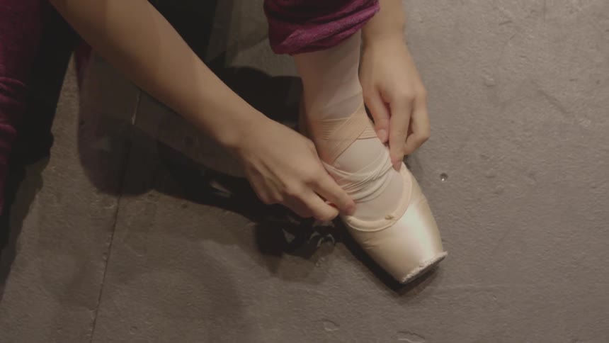 A ballerina ties her ballet shoe