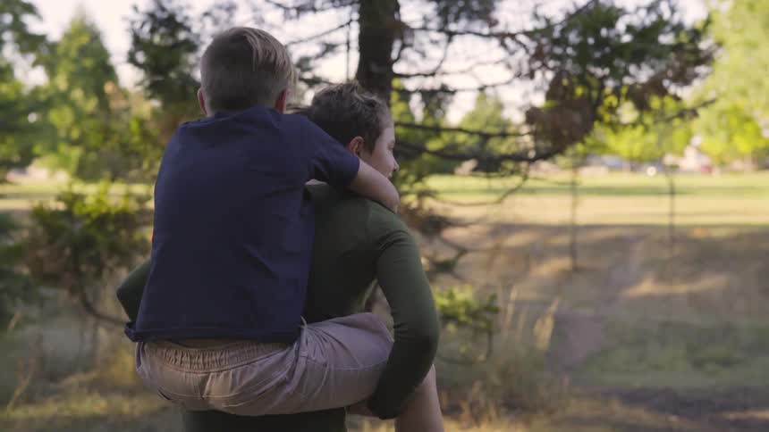 Boy gives a piggyback ride to another boy outside on a sunny day