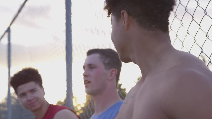 Teenagers smile and lean against a chain link fence