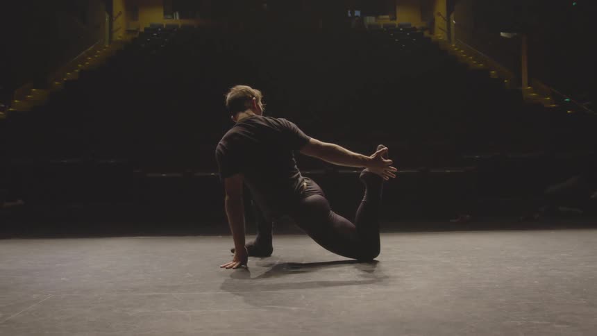 A male dancer stretches on stage