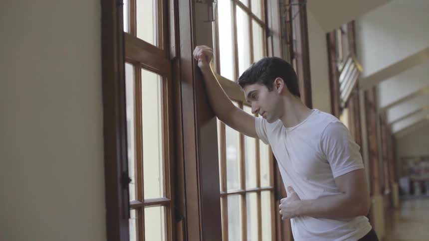 Man leans against the window frame as he looks outside