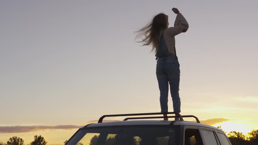 Woman stands on top of a vehicle at sunset