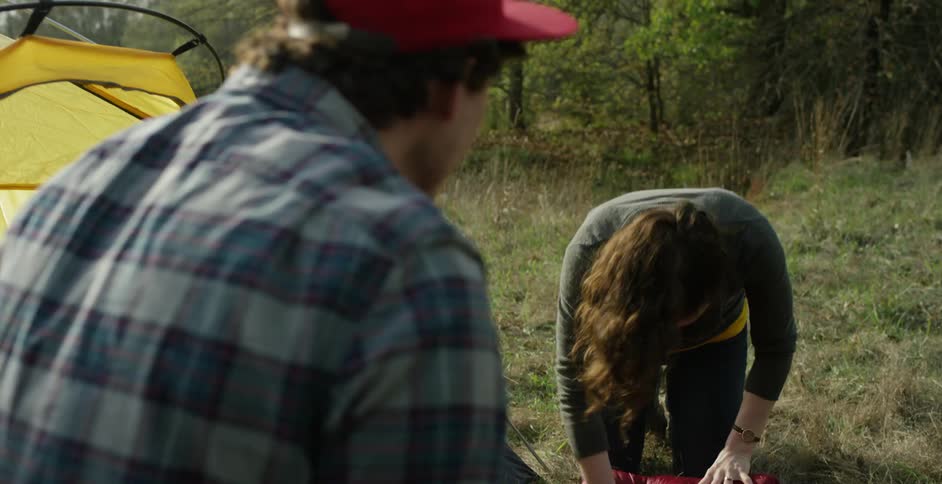 A man and woman fold up their gear at a campsite