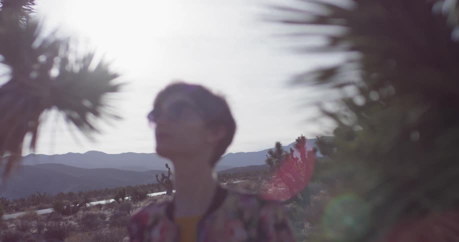 A woman stands next to plants in a desert