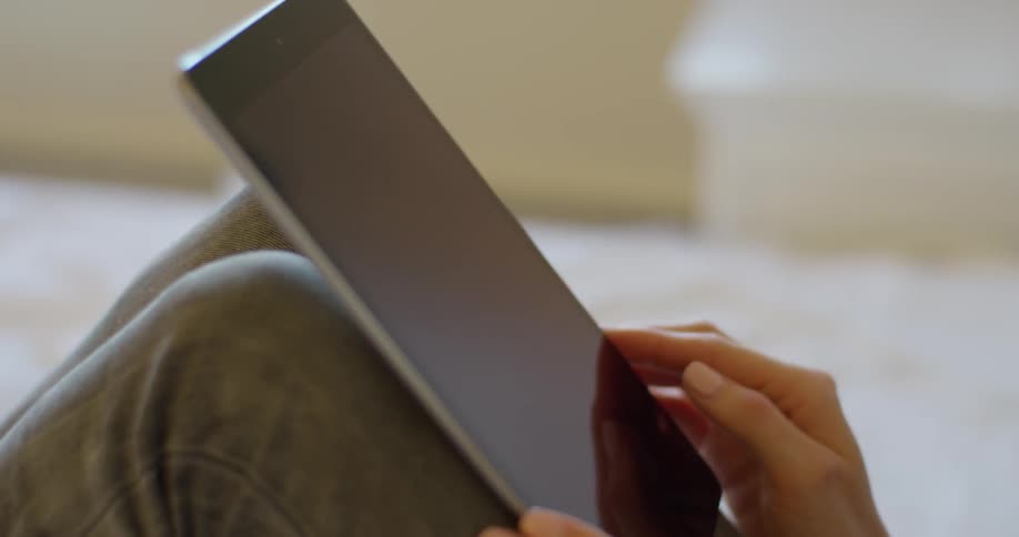 Woman taps and scrolls on her tablet as she sits with her knees bent