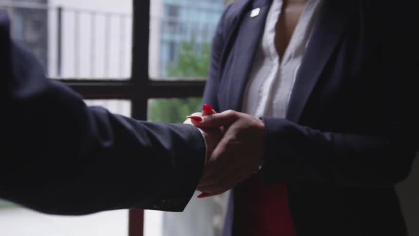 Two business professionals shake hands in front of a window
