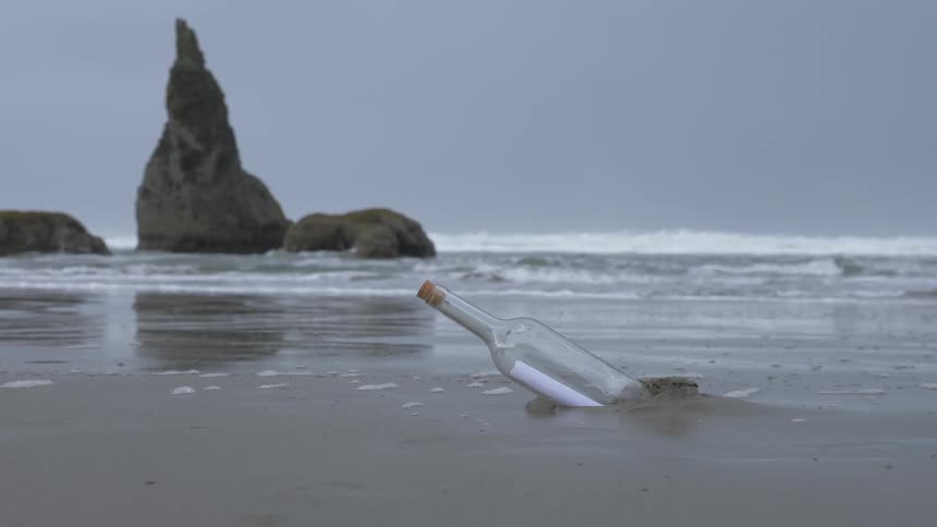A glass bottle with a note inside sits on a sandy beach