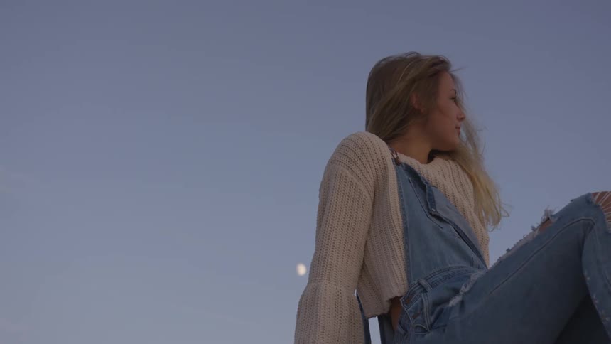 Woman in denim overalls sits under the blue sky