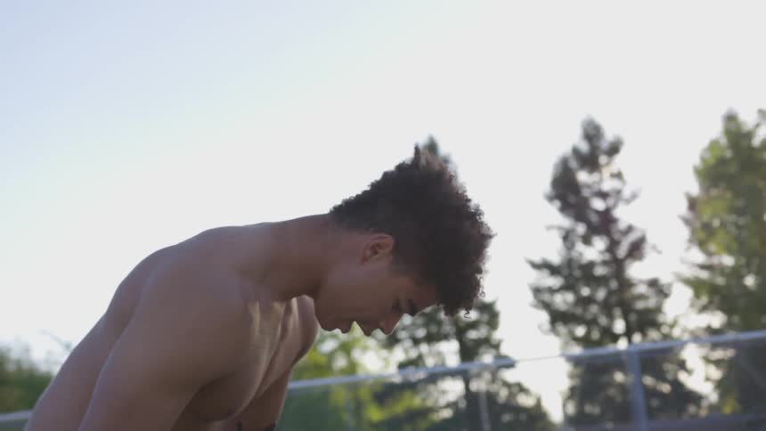 Two young men play basketball in a park at sunset