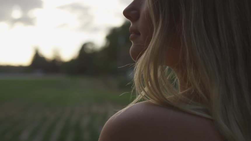 A woman stands on a farm at sunset