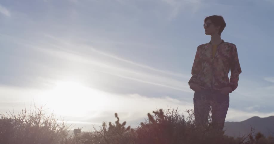 Woman stands outside in tall grass on a sunny day