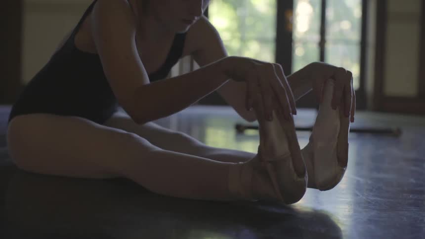 Ballerina is stretching her legs and feet on floor