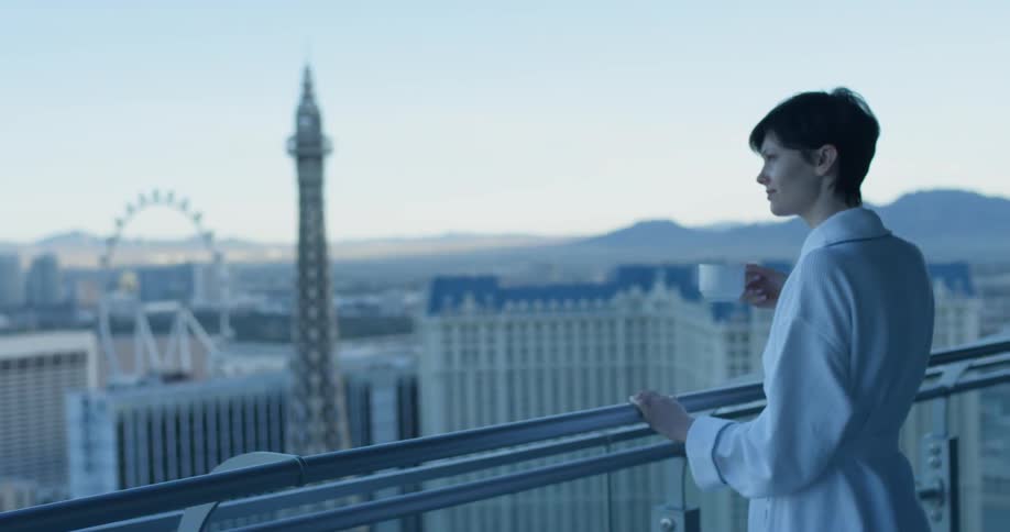 A woman stands on the balcony drinking from a mug