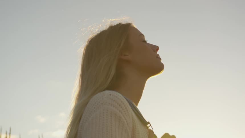 A woman stands outside with her eyes closed at sunset