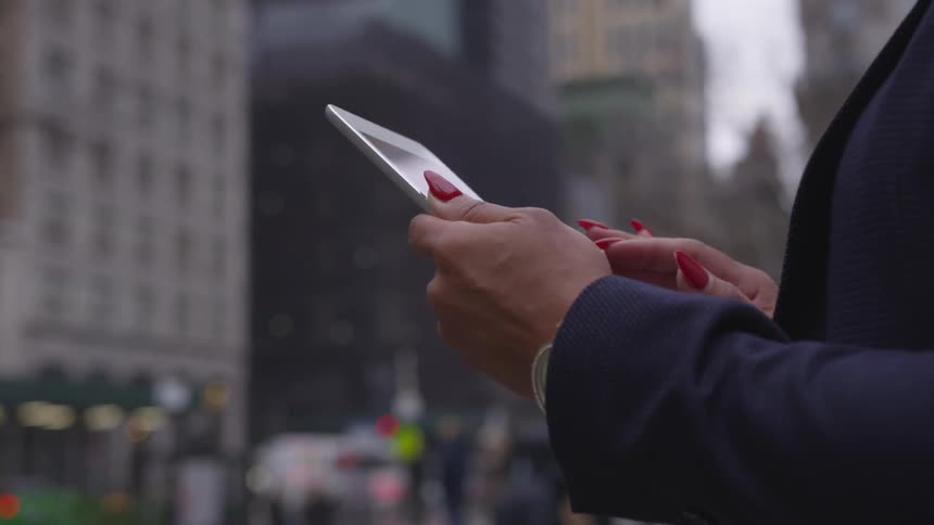 A woman scrolls on a tablet on a city sidewalk