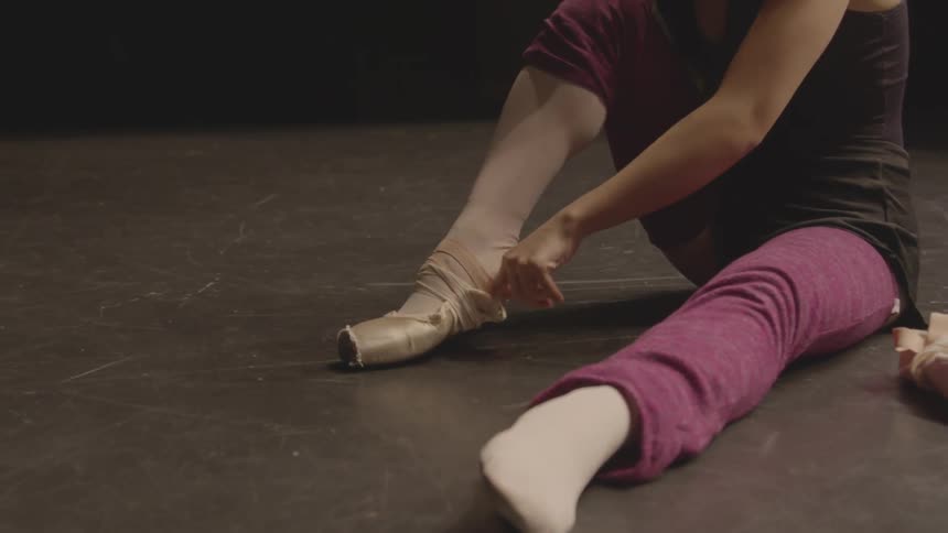 A ballerina puts on ballet shoes