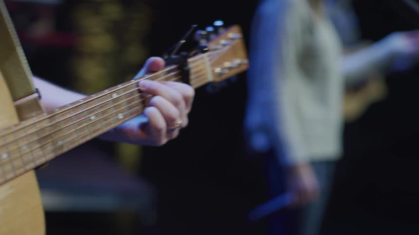 A guitarist is swaying and pacing as he stands on a stage