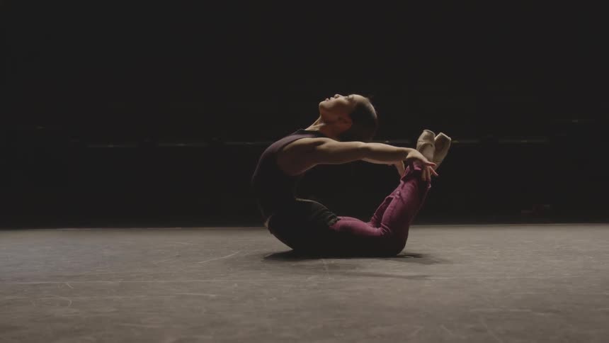 A woman lays on the floor in the dark doing a deep back stretch