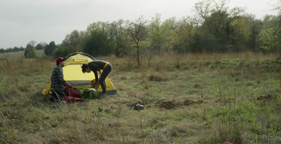 A young couple playfully packs up their campsite in the forest