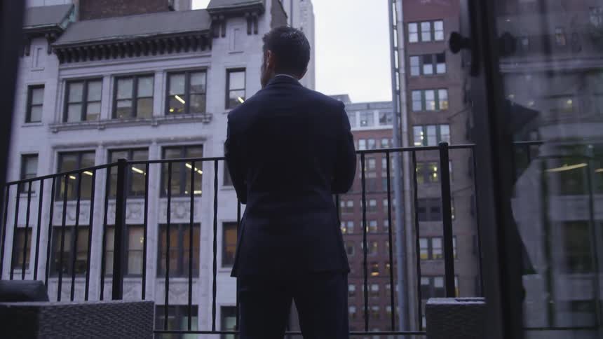 A man stands on the balcony looking at the city