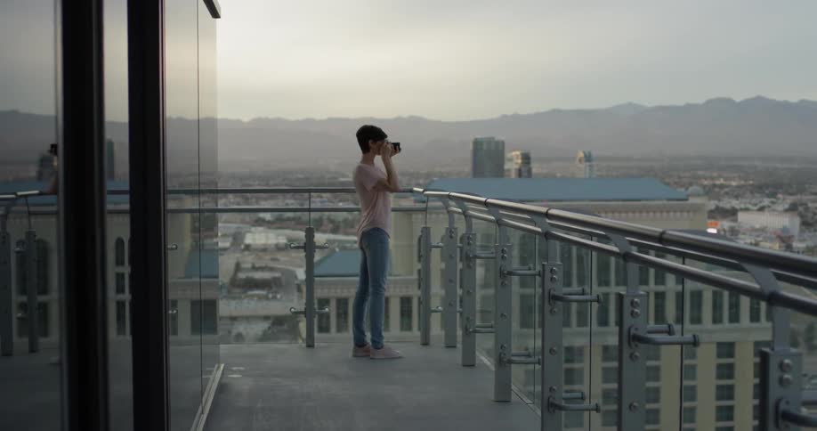 Woman takes a picture of a city while standing on a balcony