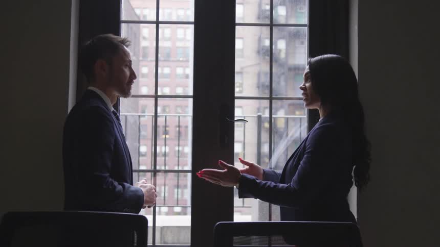 Man and woman wearing suits talking in front of a large window