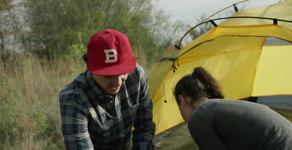 A man and woman packing up a campsite beside a yellow tent