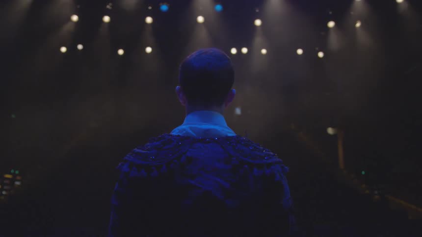 Man stands on stage with lights shining on him