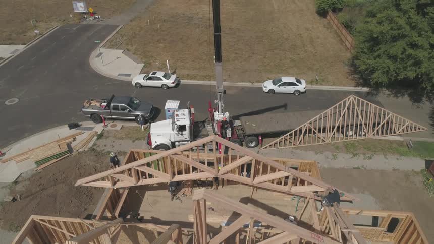 A roof joist is being placed by a crane onto a construction project in daylight