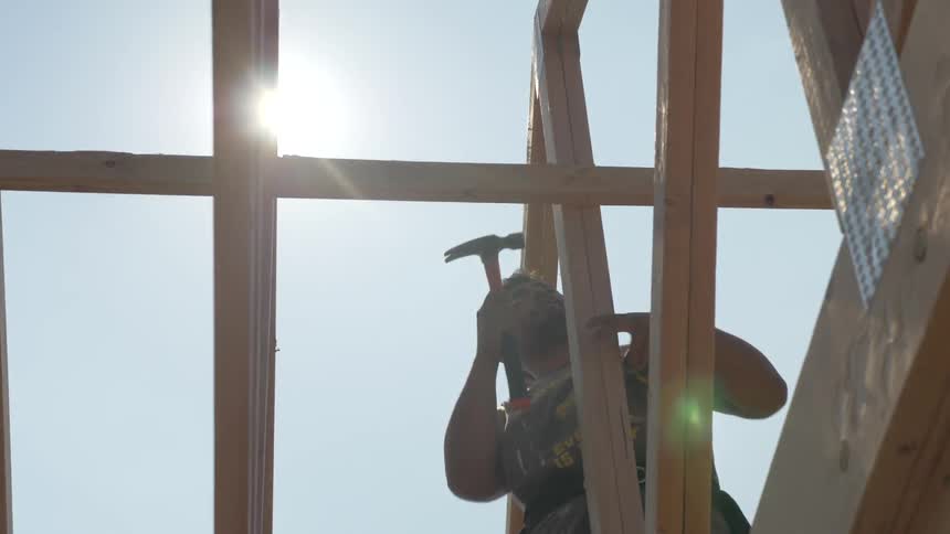 A man hammers nail into the lumber of house framing