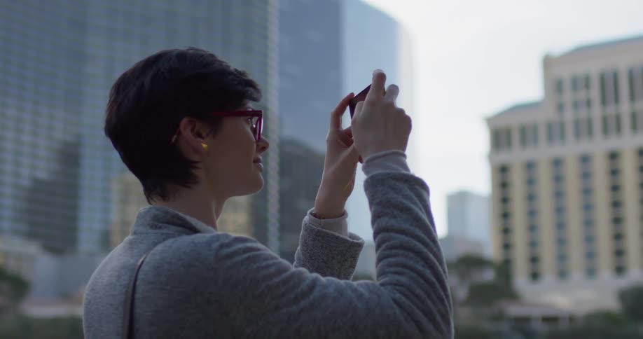 A woman stands outside taking photos of large buildings with her camera
